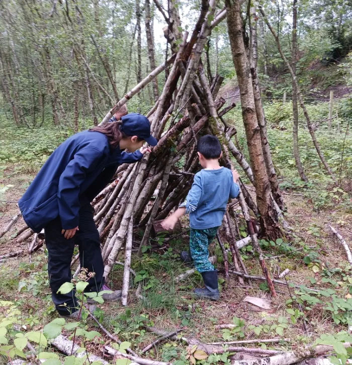 Child walks into Den as forest school leader stands by