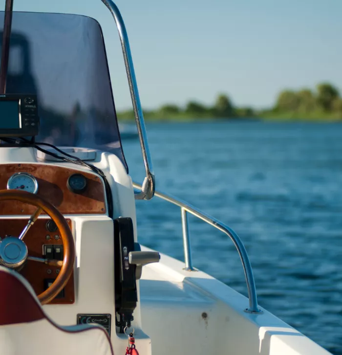 View of half a boat as it sails on the sea. The steering wheel is visible but no one is driving