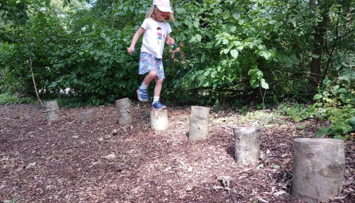 Child jumping on logs at forest school