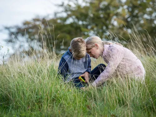 Two children outdoors in long grass using a magnifying glass.