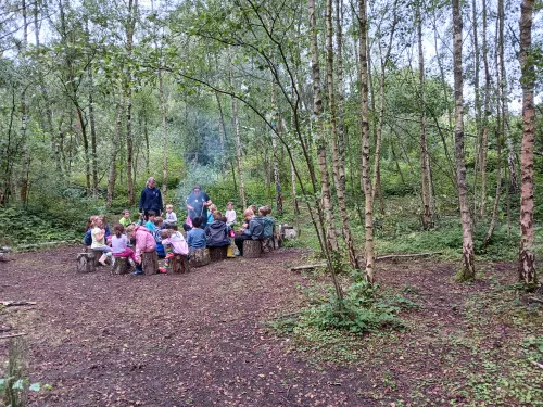 Forest school kids gather round a fire with the leader standing in the middle